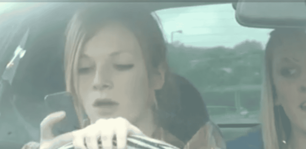 Driver looking at a mobile phone while holding the steering wheel.